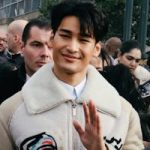 Smiling man among a crowd on a lively Paris street, capturing modern fashion and public event atmosphere.